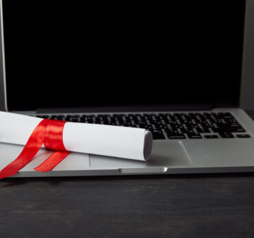 Diploma with red ribbon on laptop with blank screen on textured surface