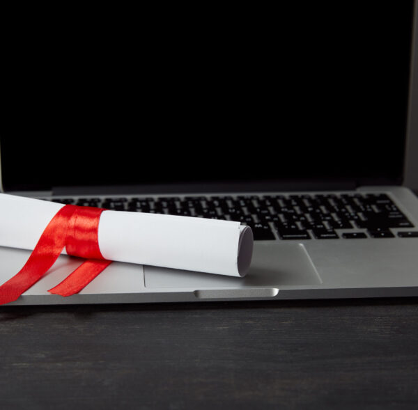 Diploma with red ribbon on laptop with blank screen on textured surface
