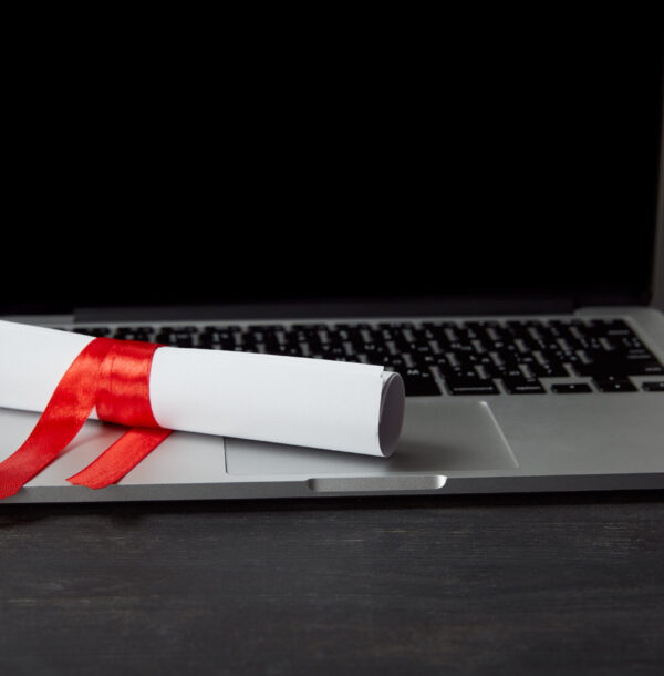 Diploma with red ribbon on laptop with blank screen on textured surface