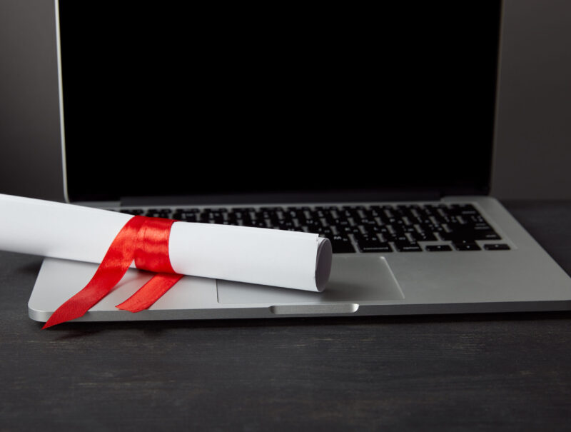 Diploma with red ribbon on laptop with blank screen on textured surface